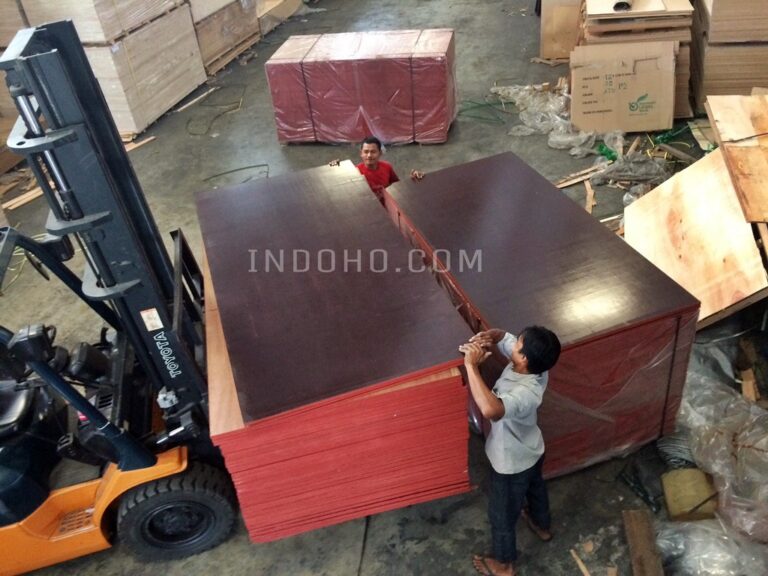 Forklift mengangkat tumpukan plywood phenolic film face di gudang distributor untuk persiapan pengiriman ke proyek konstruksi.